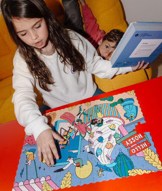 Fille avec le puzzle "Ice Cream Day" assemblé sur une table devant elle et tenant la boite effet livre dans la main – photo lifestyle – Hello Hossy