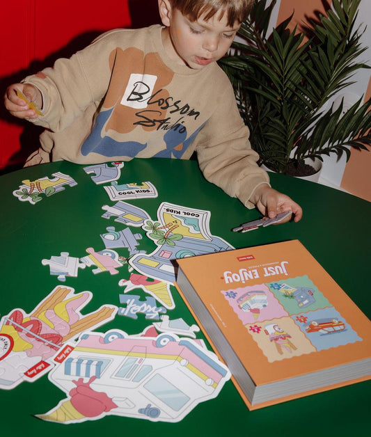 Garçon assemblant les puzzles colorés "Just Enjoy" sur une table, avec les modèles devant lui – ambiance ludique – Hello Hossy