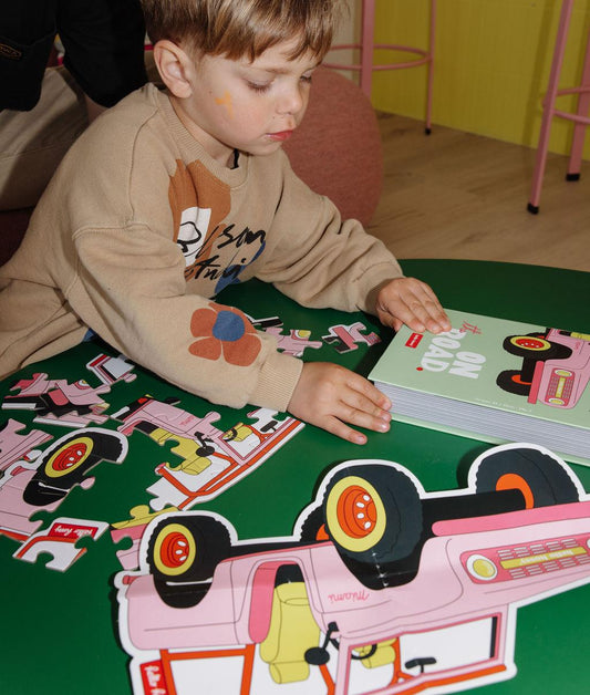 Garçon avec le puzzle "On The Road"partiellement assemblé, la boîte et l'illustration modèle, sur une table, devant lui – photo lifestyle – Hello Hossy